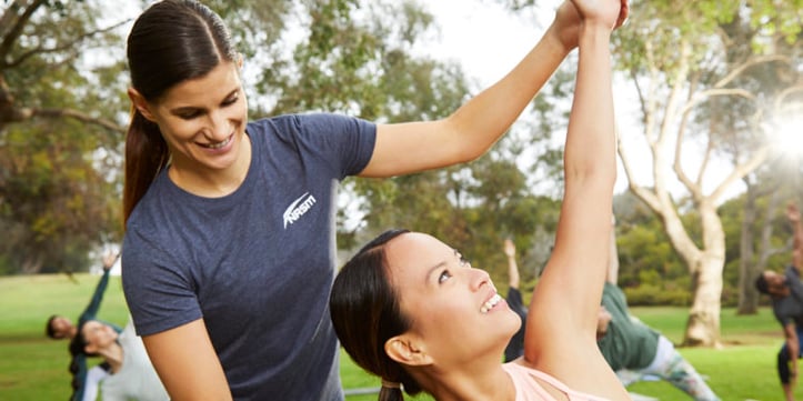 Female NASM trainer assisting client in side yoga pose