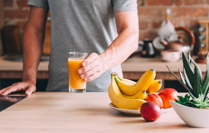 Male holding fruit juice in kitchen with fruits on counter