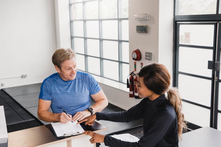 Female trainer assisting male client on filling out papers