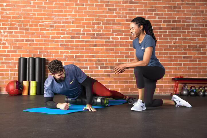 NASM Trainer assisting client with foam roller stretch on leg