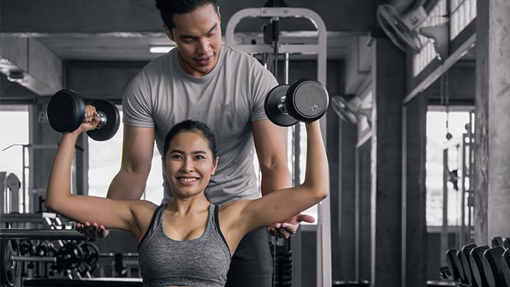 Trainer assisting client with dumbbell shoulder press