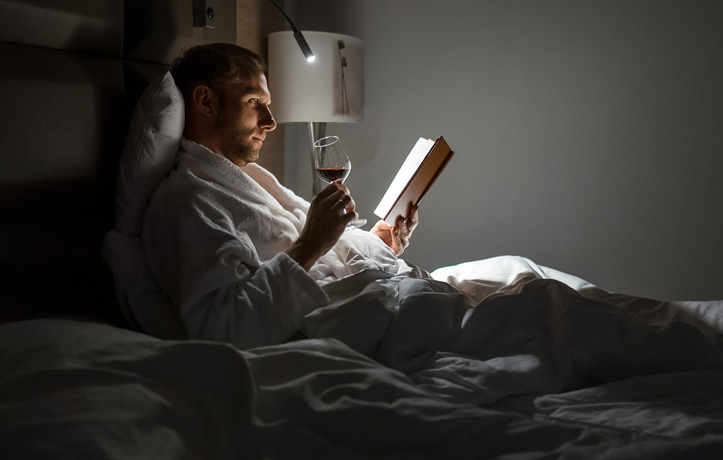 a man laying in bed with a glass of wine and a book