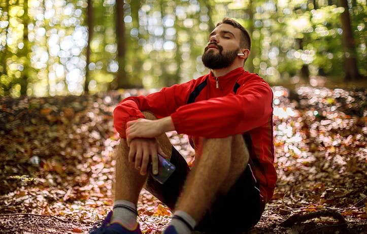 a relaxed man sitting in the forest with his eyes closed