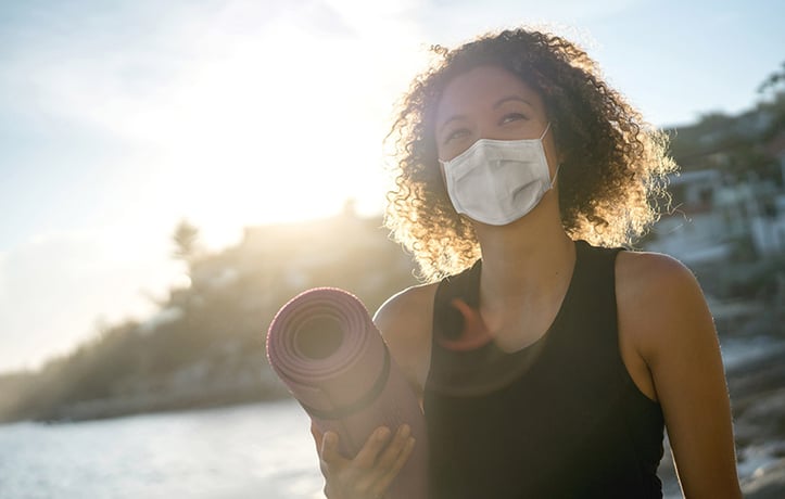 woman wearing a mask and exercising on beach after covid