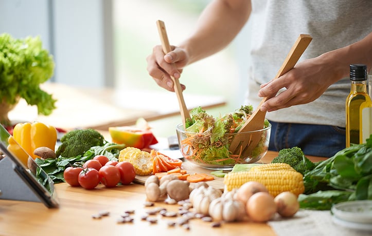 Someone making a bowl of salad with different healthy foods around