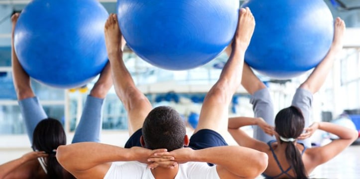 Group fitness class and people with yoga balls between feet