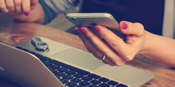 Someone typing on laptop with smartphone in hand