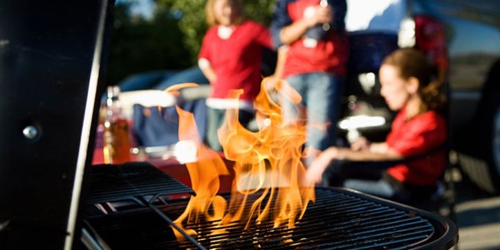 fire coming from grill with tailgate going on around