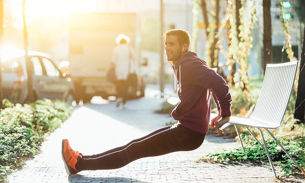 trainer doing a tricep dip on a park bench