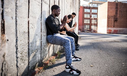 three people doing a wall sit at an outdoor gym