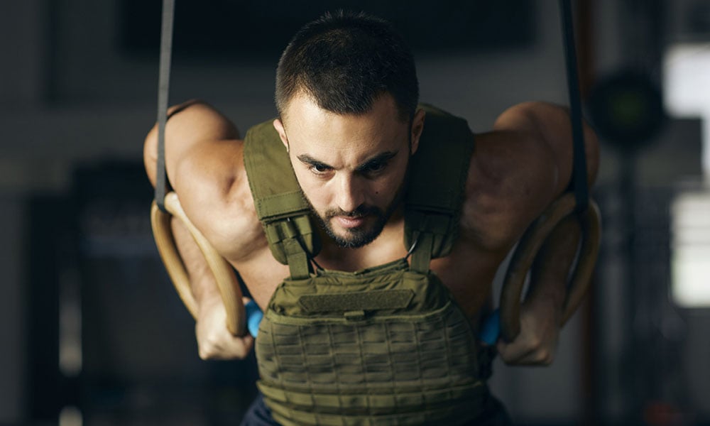 man doing ring pushups with a weight vest on