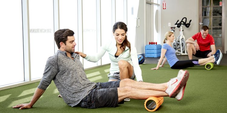 Female trainer assisting male client on foam roller
