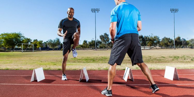 Male trainer assisting male athlete without workout drill on outdoor track