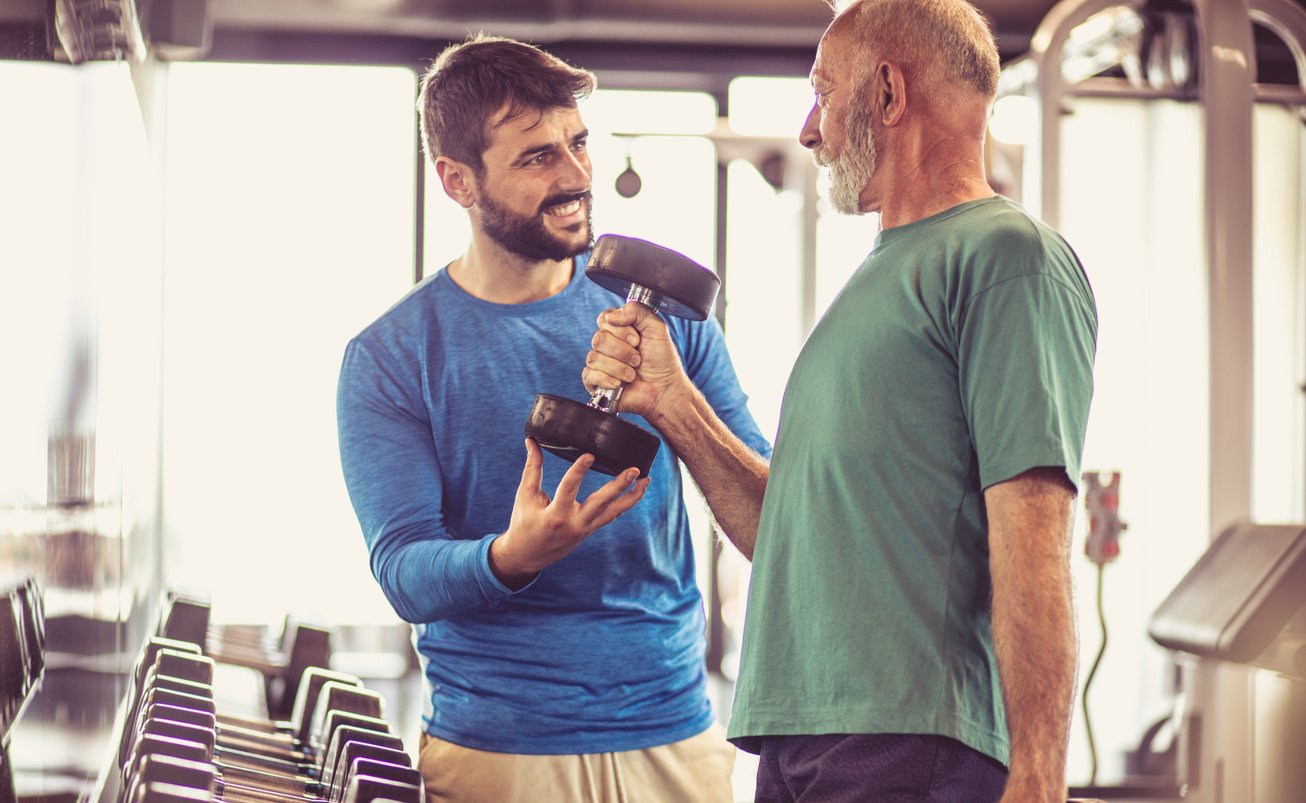 Male trainer assisting male elderly client on dumbbell hammer curls