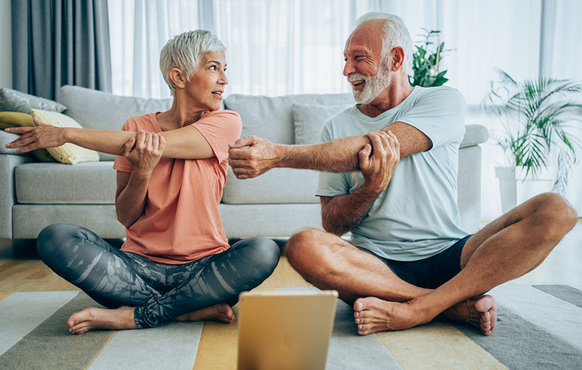 Two older adults stretching in living room