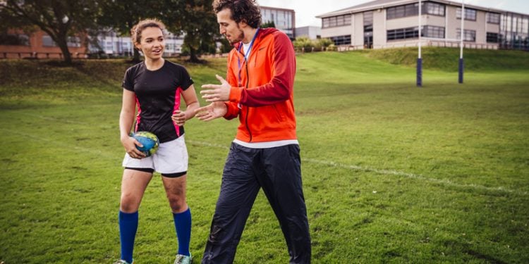 male coach assisting female athlete on field