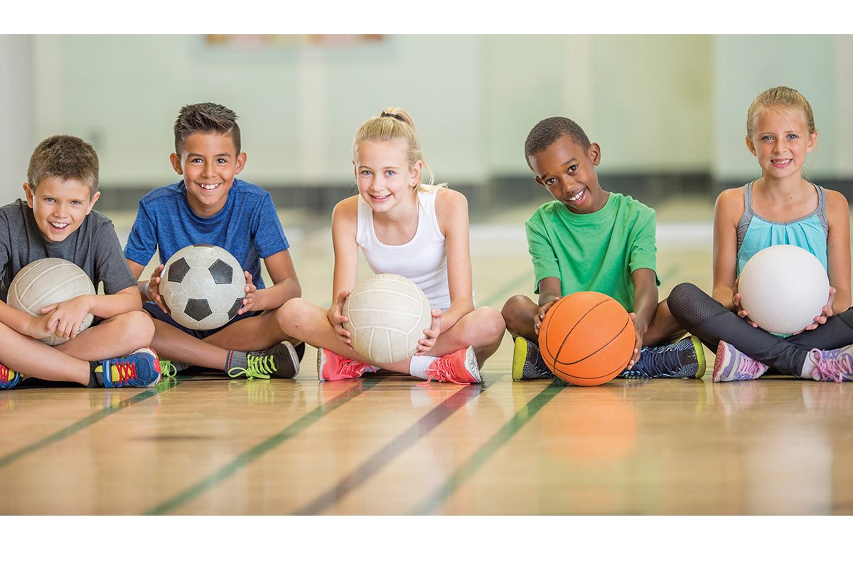 group of kids sitting on court with a variety of sport balls