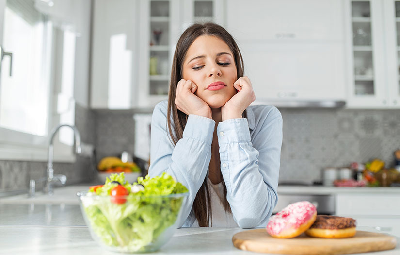 Woman standing between donuts and salad, giving the salad a unwanted look