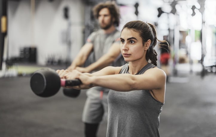 a woman and a man doing kettlebell swings in a gym