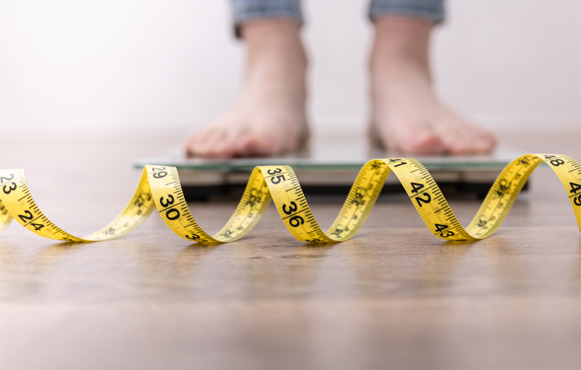 A lady stepping on the scale with a measuring tape in front