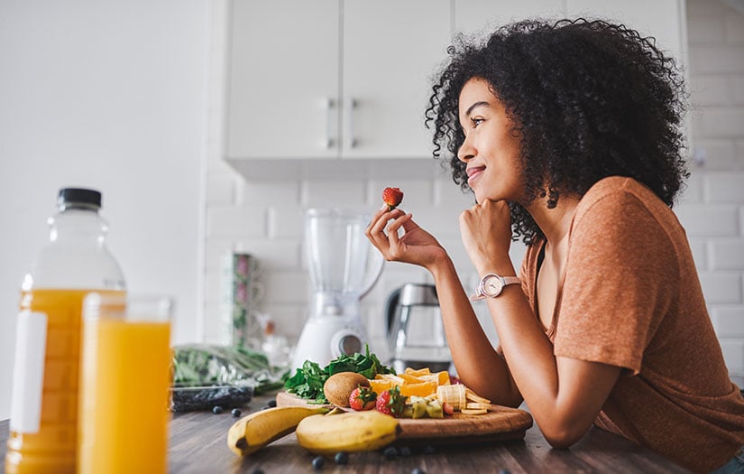 Woman eating plate of fruit in kitchen