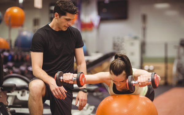 male trainer assisting female client on workout with yoga ball