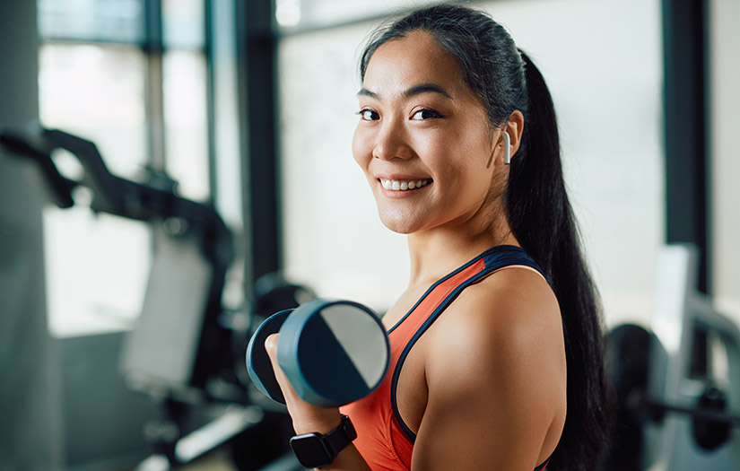 woman smiling at camera while doing a single-arm dumbbell bicep curl