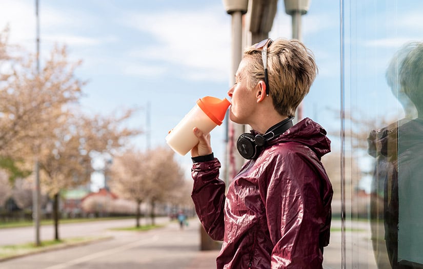 woman drinking protein shake out of an orange shaker